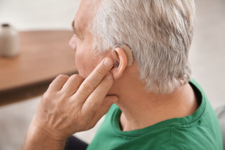 Senior man adjusting his hearing aid. 